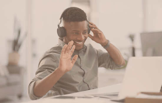 Smiling man wearing headphones waving at his laptop during a video call, symbolizing high-performing professionals needing quick nervous system resets between meetings.