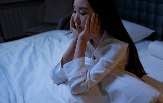 Woman sitting awake in bed at night, looking anxious and unable to sleep.