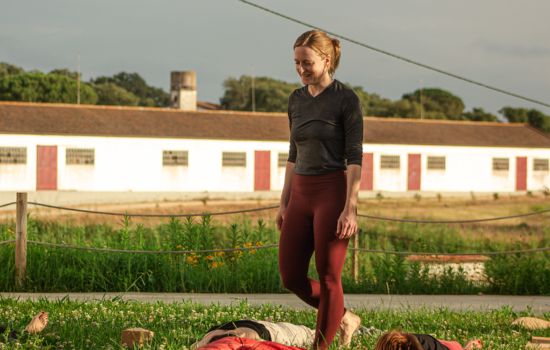 Sleep and neuro performance coach teaching a calming outdoor yoga class, representing energy recovery and nervous system awareness after a restless night.